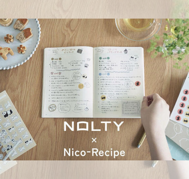 Flat lay of notebooks, washi stickers, and sticky notes from the NOLTY × Nico-Recipe stationery collaboration, featuring warm stamp-style designs for journaling, planning, and everyday writing.